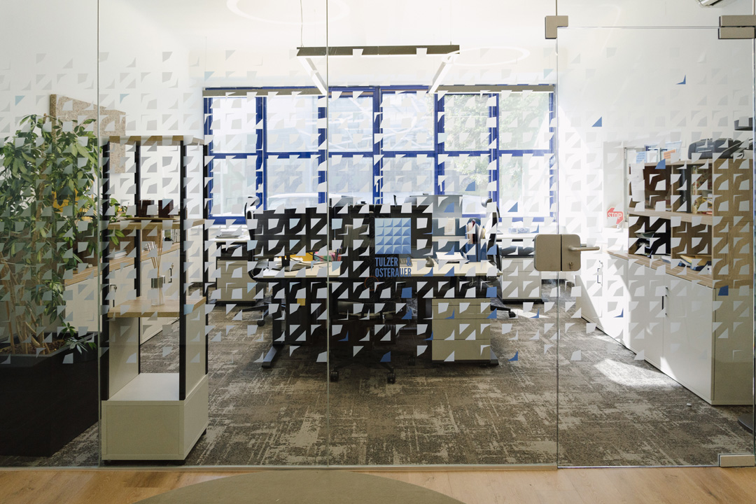 Büro Tulzer & Osterauer: Modernes Bürodesign mit Glaswand und Arbeitsplatz.
